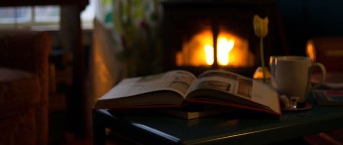 Book and cup of coffee next to a warm fireplace