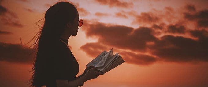 teen girl reading book on beach at sunset