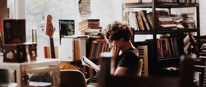 a girl reading a book in her room (also filled with books)