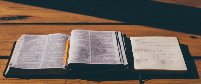 an open notebook and pencil alongside a book on wooden table