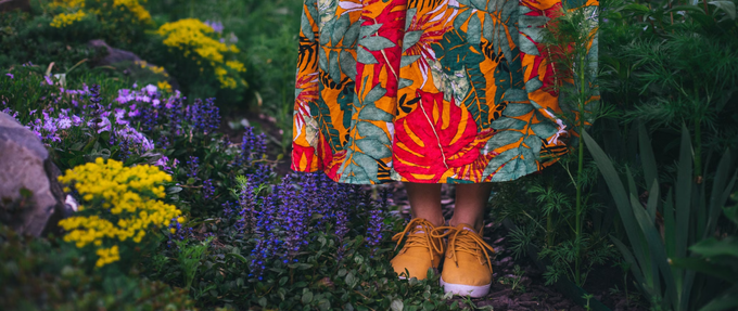 woman's orange sneakers and colorful skirt standing amongst purple and yellow flowers
