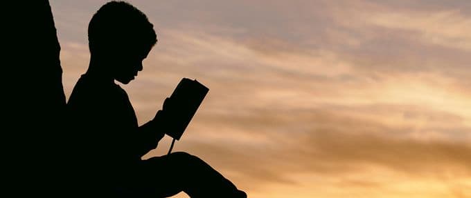 silhouetted child reading a book at sunset
