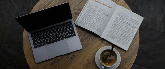 Photograph of a laptop, an open magazine, and a cup of coffee on a round table.